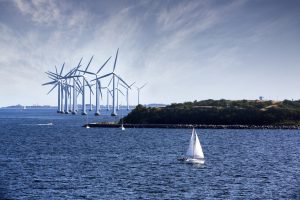 Big group of wind turbines on the bay with a small sailboat sailing in the foreground.